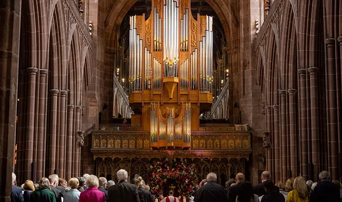 Congregation gathered in cathedral nave facing ornate golden pipe organ above the altar.