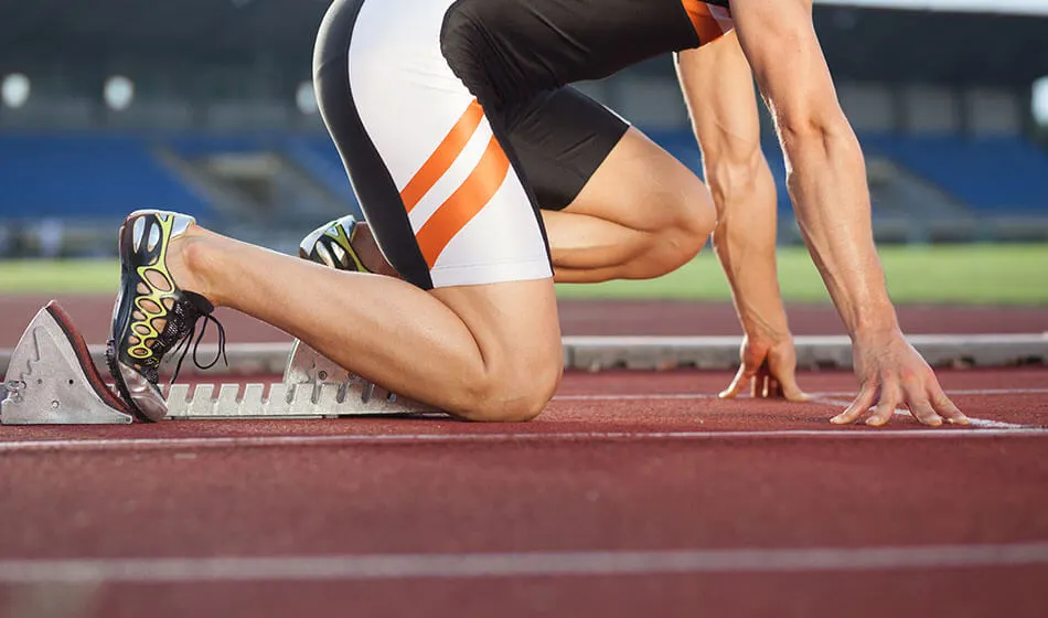 Athlete in sprinting position at starting blocks on a running track.
