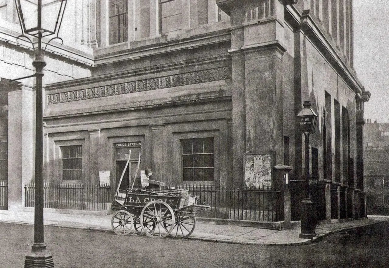 Historic street corner showing a stone police station building with a hand-drawn cart parked outside.