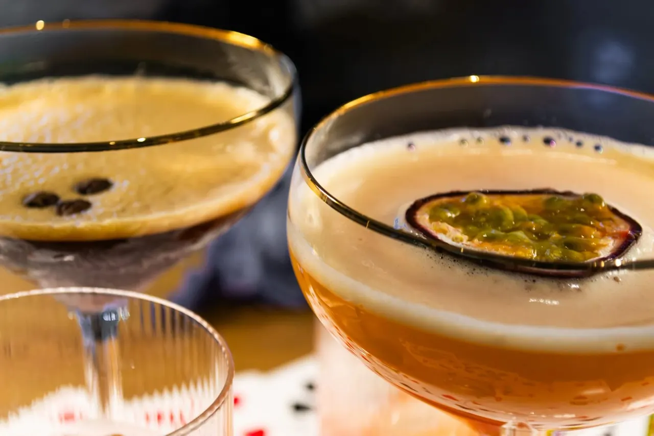 Close-up of three cocktails with foamy heads and garnishes including what appears to be a passion fruit slice.