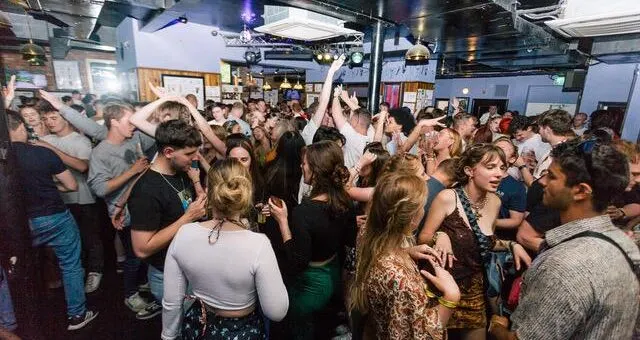 Large crowd of people dancing together in an indoor venue with stage lighting.
