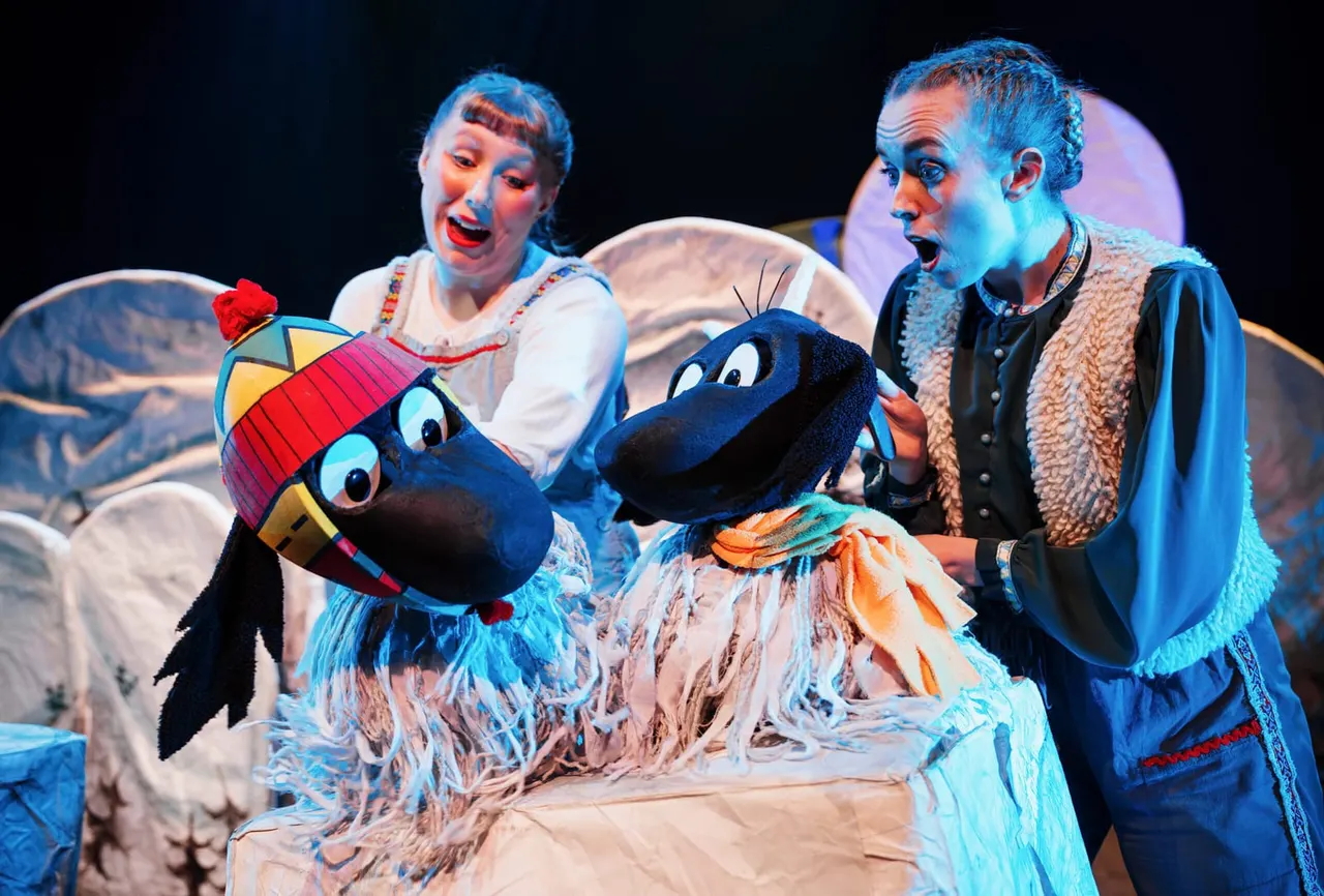 Two actors in traditional costumes perform with puppet birds on stage under theatrical lighting.