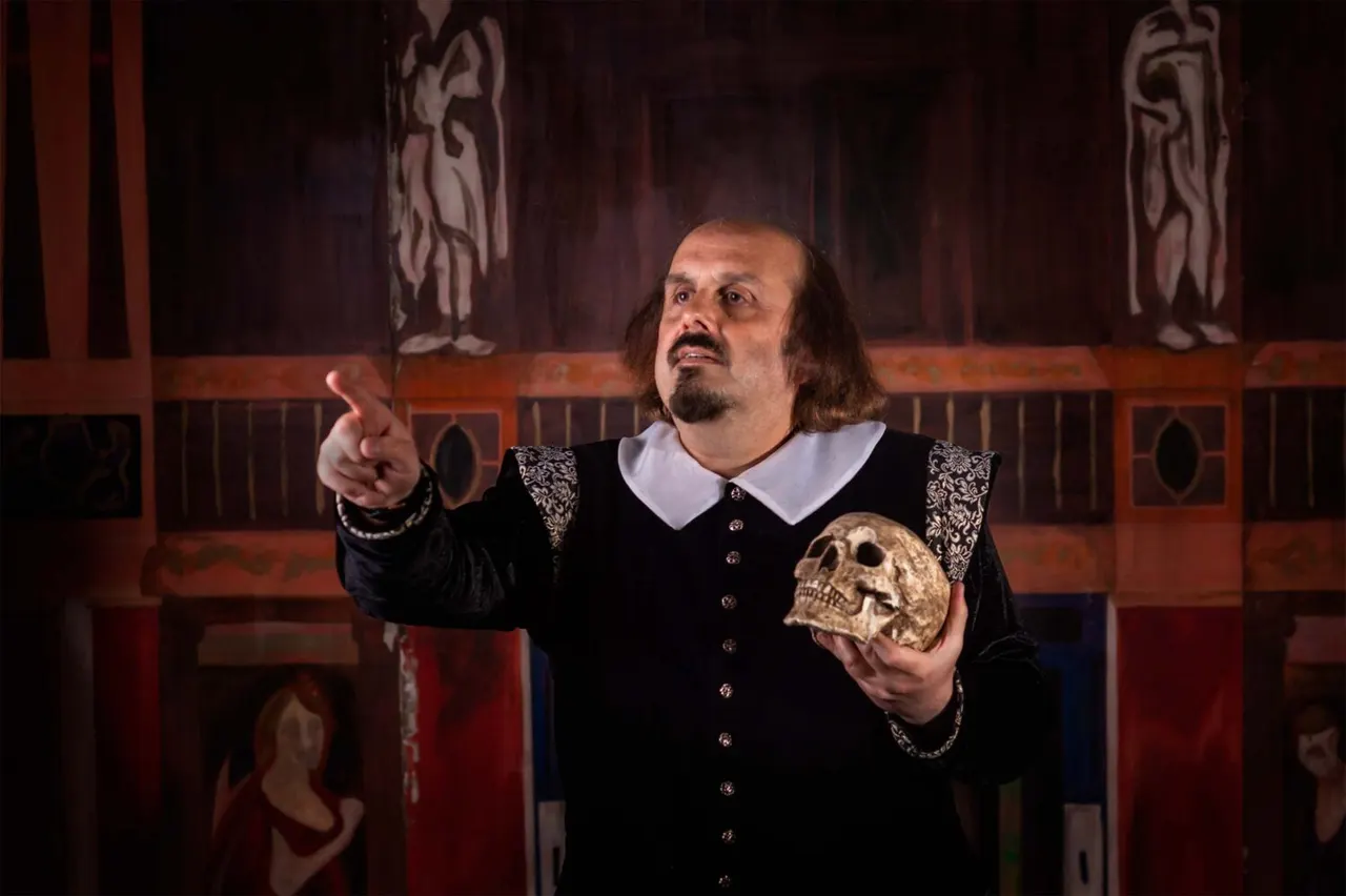 Actor in Elizabethan costume holding a skull on a theatre stage set.