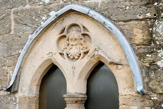 This is a PHOTOGRAPH, not a designed graphic.

Ornate stone archway with carved decorative head above two rounded window openings at a historic castle.