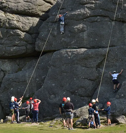 Person rock climbing on a large granite rock face with instructors and participants belaying below.