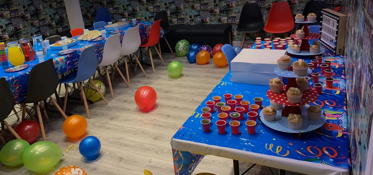 Children's party room set up with colourful balloons, decorated tables, cupcakes, drinks and modern chairs.