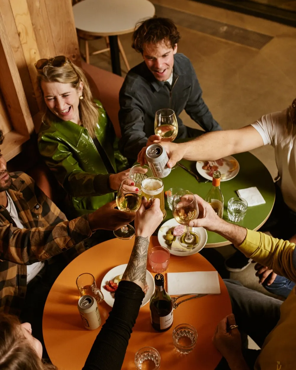 Friends toasting with drinks and sharing food at a table during a social gathering indoors.