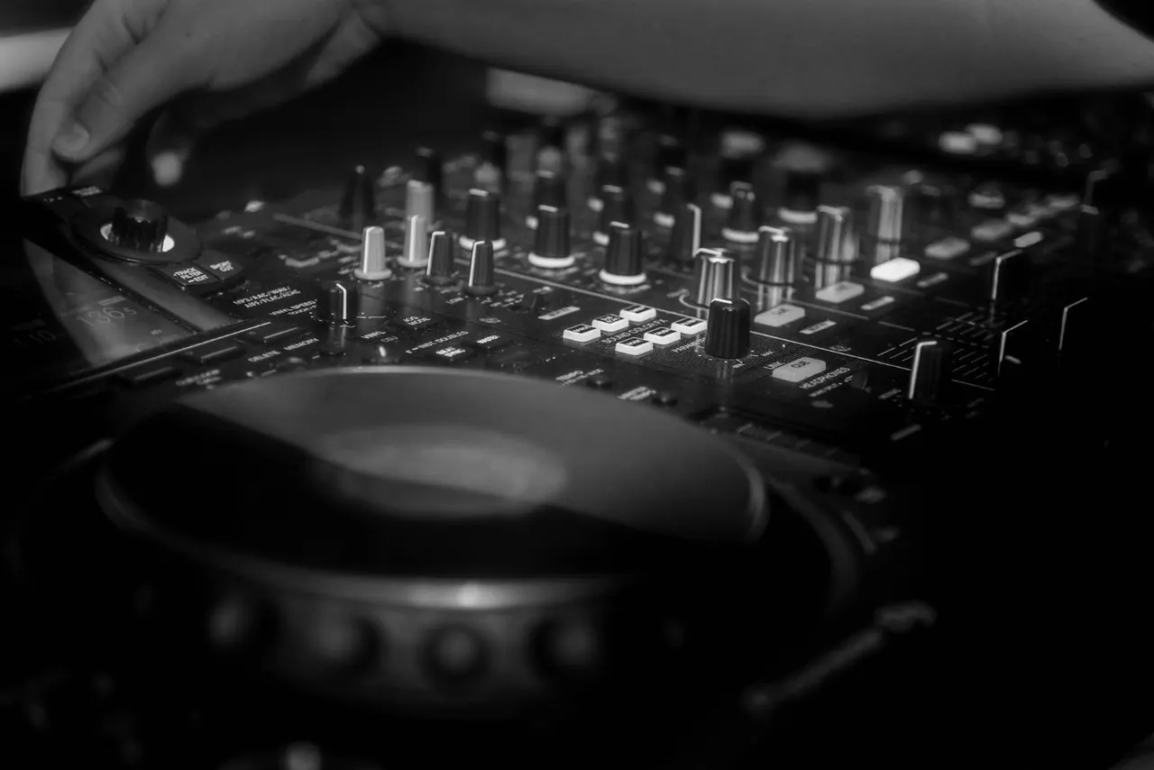 DJ operating a mixing console with headphones around their neck during a performance.