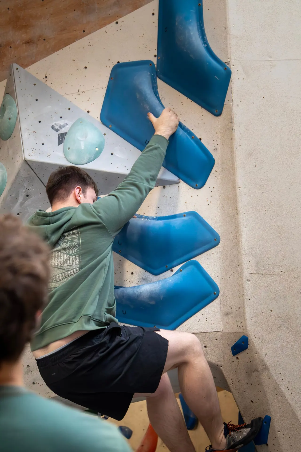 Young person climbing an indoor bouldering wall with blue plastic handholds.