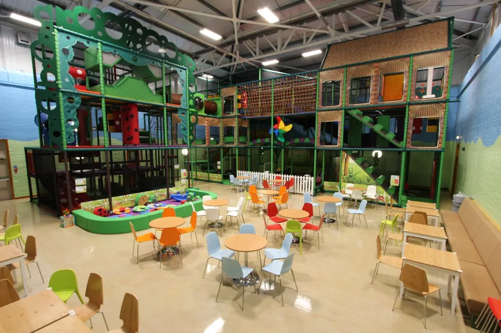 Indoor soft play centre with colourful multi-level climbing structures, activity tables and seating for young children.