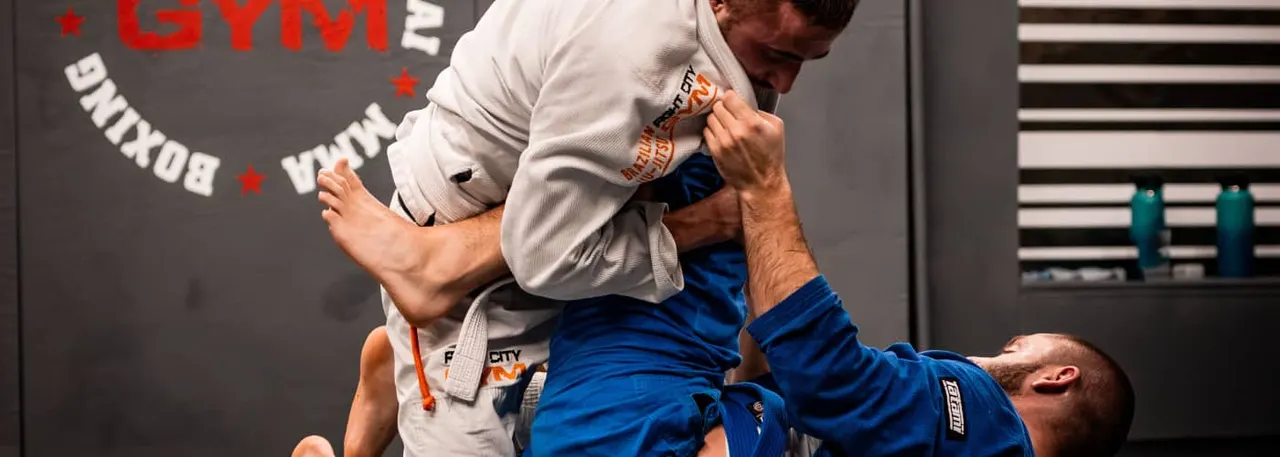 Two men grappling during a jiu-jitsu or martial arts training session on a gym mat.
