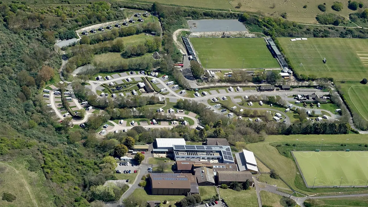 Aerial view of a caravan and motorhome campsite with pitches, sports fields, and surrounding woodland.
