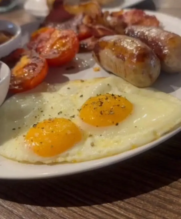 Cooked breakfast plate with two fried eggs, grilled tomato halves and mushrooms.