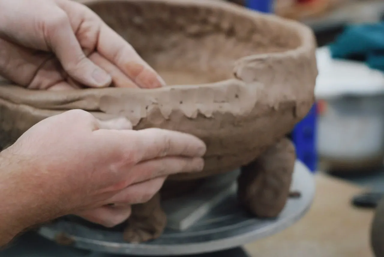 Child's hands shaping wet clay on a pottery wheel during a workshop.