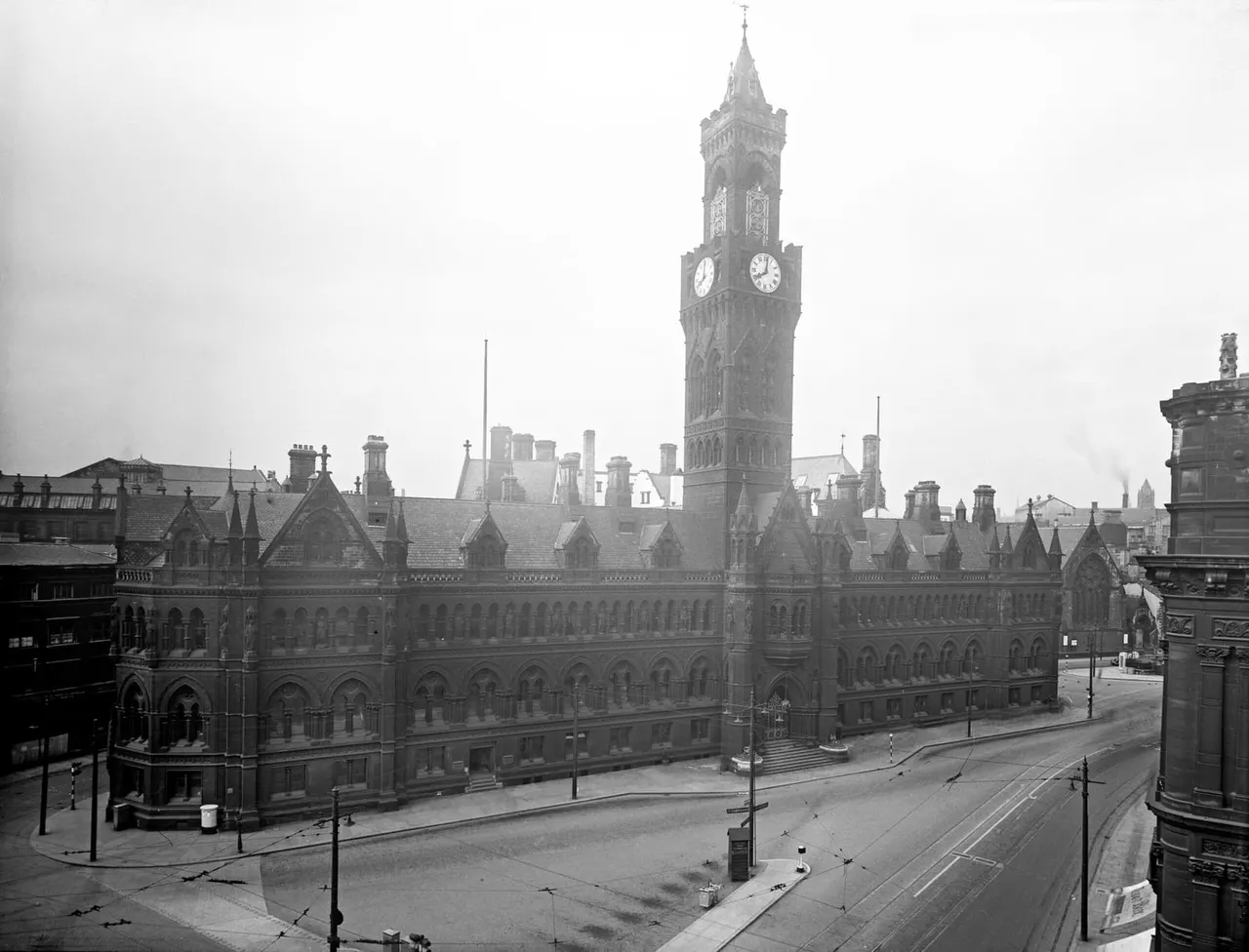 Victorian Gothic Revival town hall with prominent clock tower overlooking an empty city square in black and white.