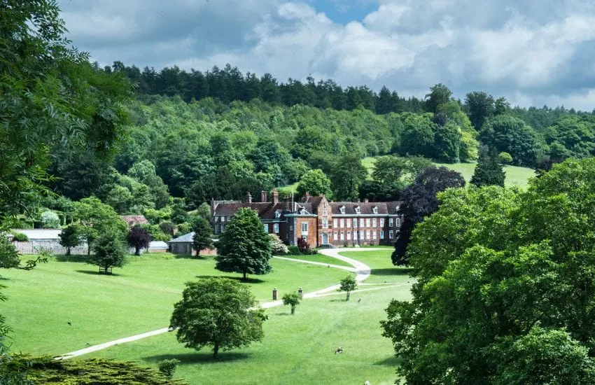 Georgian country house set in extensive green grounds with tree-lined hills and winding pathways.