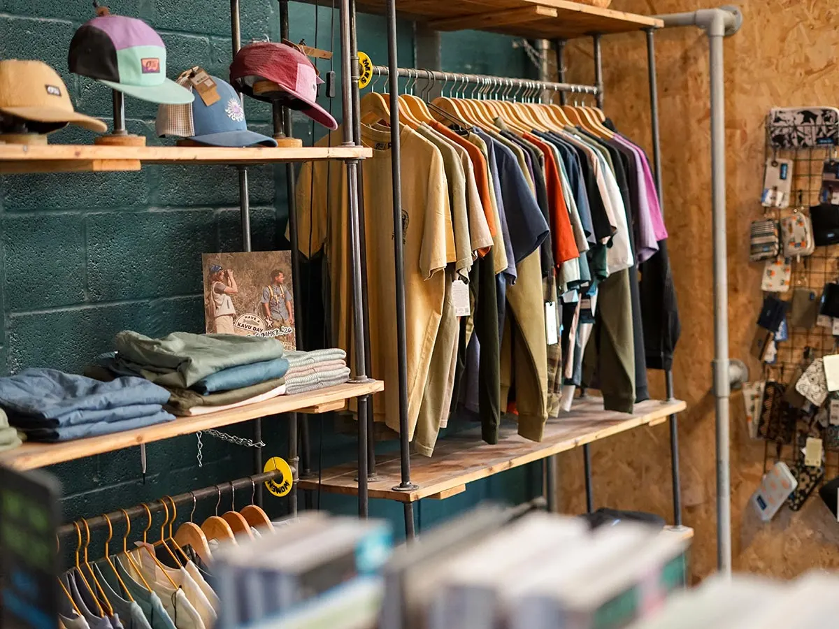 Clothing and accessories displayed on wooden shelves and rails in a retail shop interior.