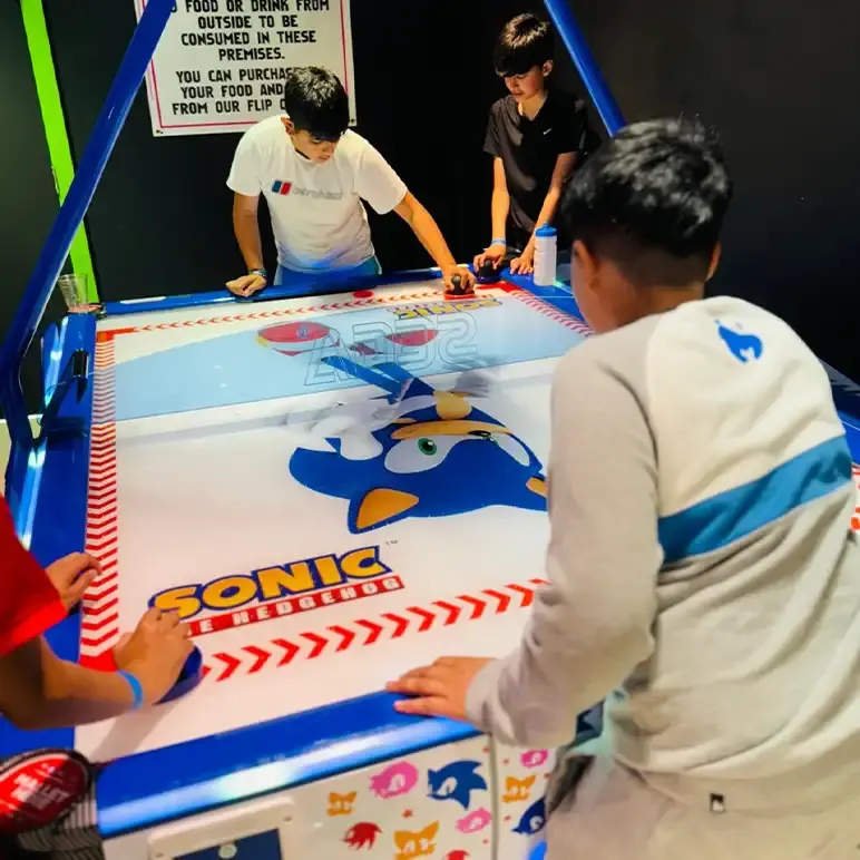 Children playing air hockey at an indoor leisure venue, with staff members supervising.