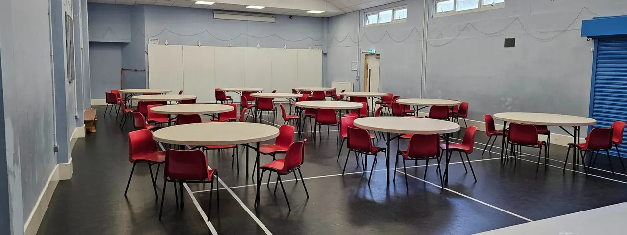 Large community hall with round tables and red chairs arranged for group activities or dining.