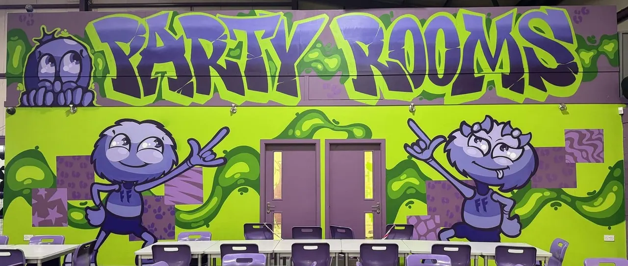 Colourful mural with lime-green background, purple cartoon characters and graffiti-style text above double doors in an indoor play venue.