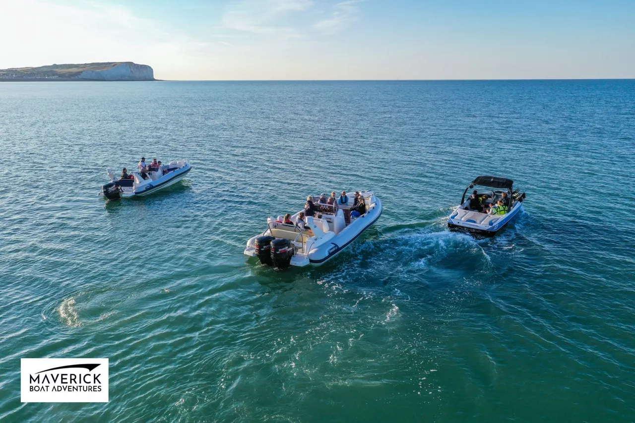 Three speedboats with passengers in clear blue-green coastal waters, with white cliffs visible on the horizon.