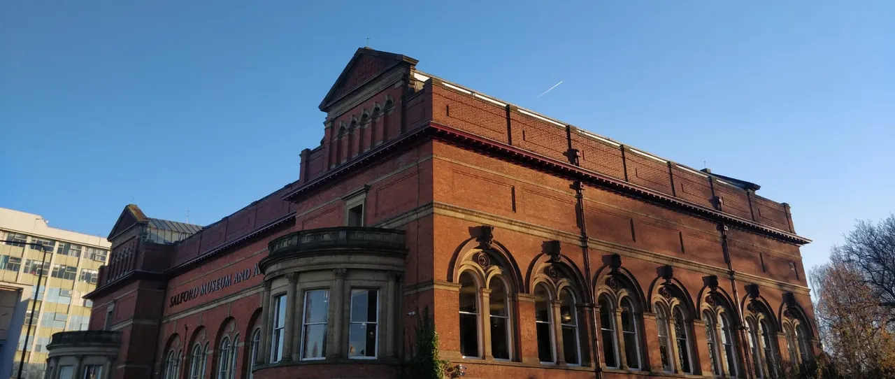 Victorian red-brick building with ornate arched windows and a dark roof against a clear blue sky.