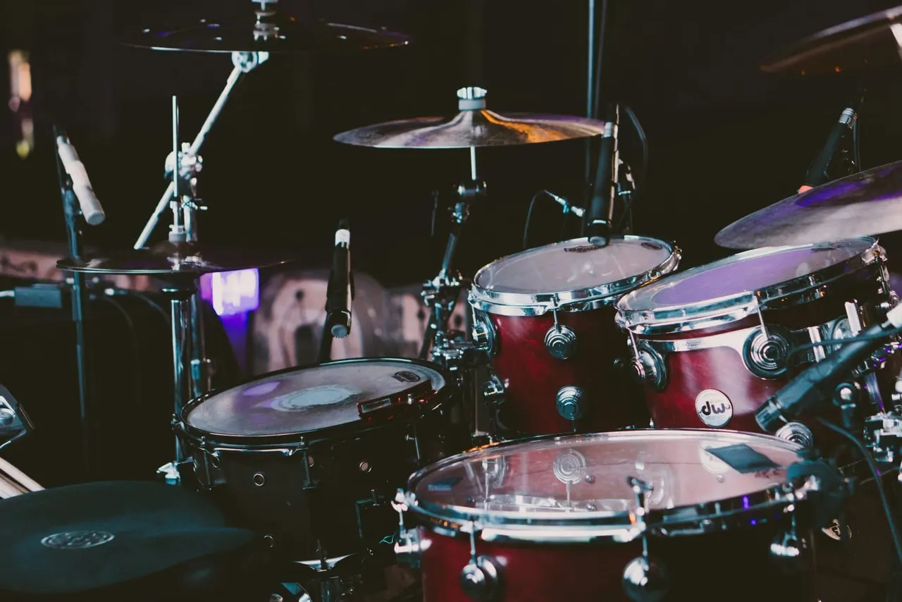 A drum kit with red and burgundy drums, cymbals, and hardware set up on a dark stage with purple lighting.