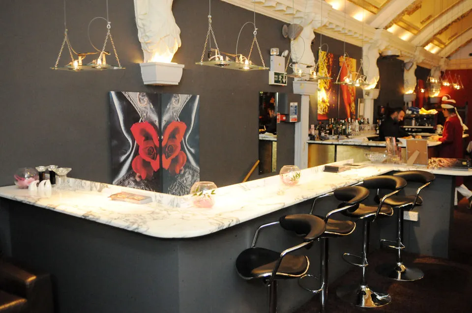 Modern bar counter with marble top, black stools, suspended lighting, and red artwork on dark wall.