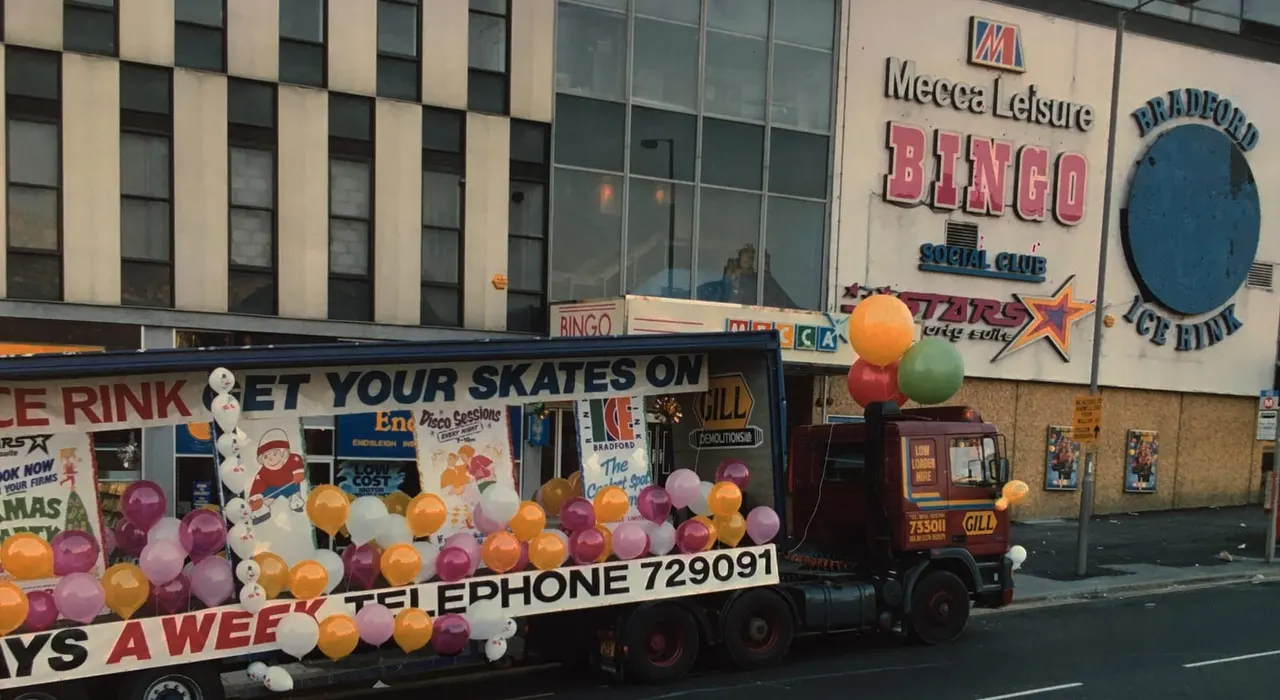Decorated carnival float with colourful balloons parked outside Bradford ice rink and bingo hall buildings.