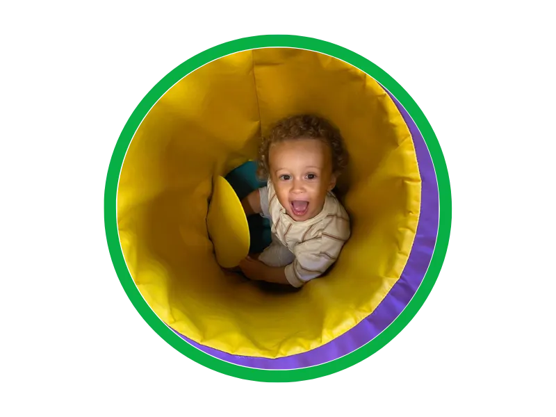 Young child crawling through a yellow fabric tunnel with green and purple trim.