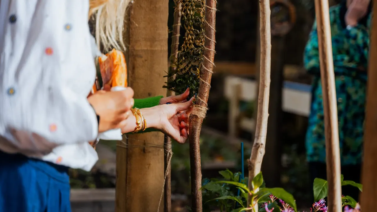 Person touching moss-covered wooden post in a garden setting with flowering plants nearby.