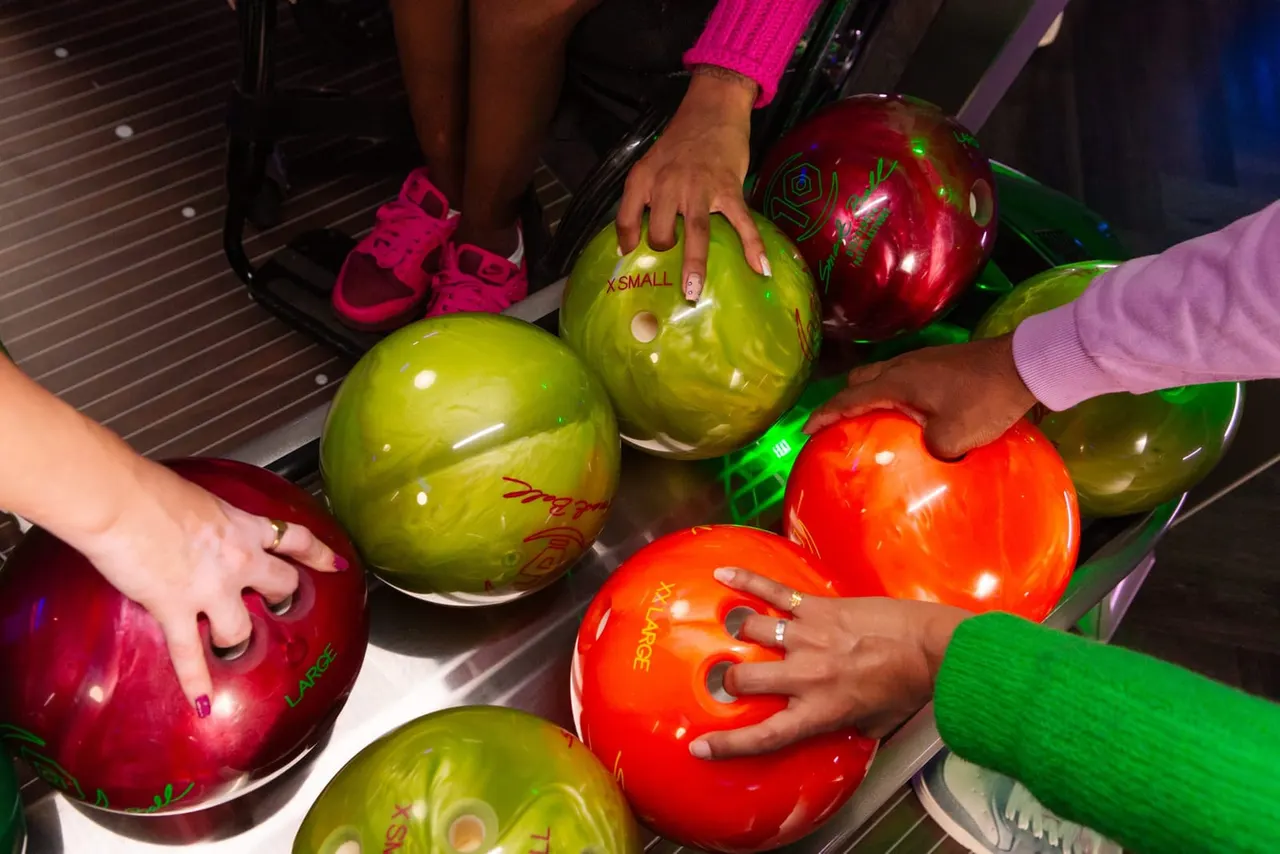 People selecting bowling balls in various colours at a bowling alley.