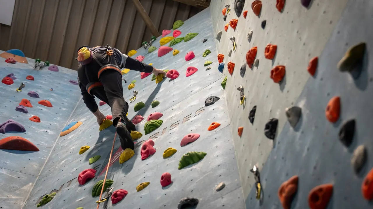 Person rock climbing on an indoor wall with colorful hand and foot holds.