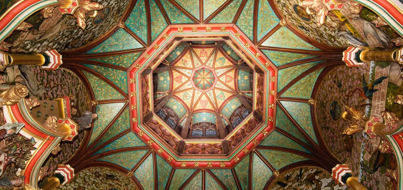 Ornate ceiling with turquoise panels, gold leaf detailing, red borders and geometric patterns inside a historic castle chamber.