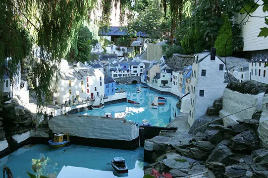 Miniature seaside village model with blue water, white buildings, and boats nestled among rocks and vegetation.