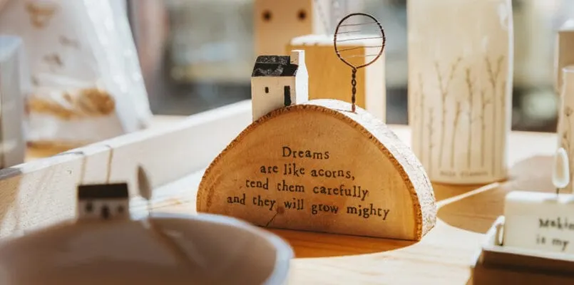 Wooden craft items and decorative pieces displayed on a shelf, including a wood-slice with inspirational text and small wooden house figurines.