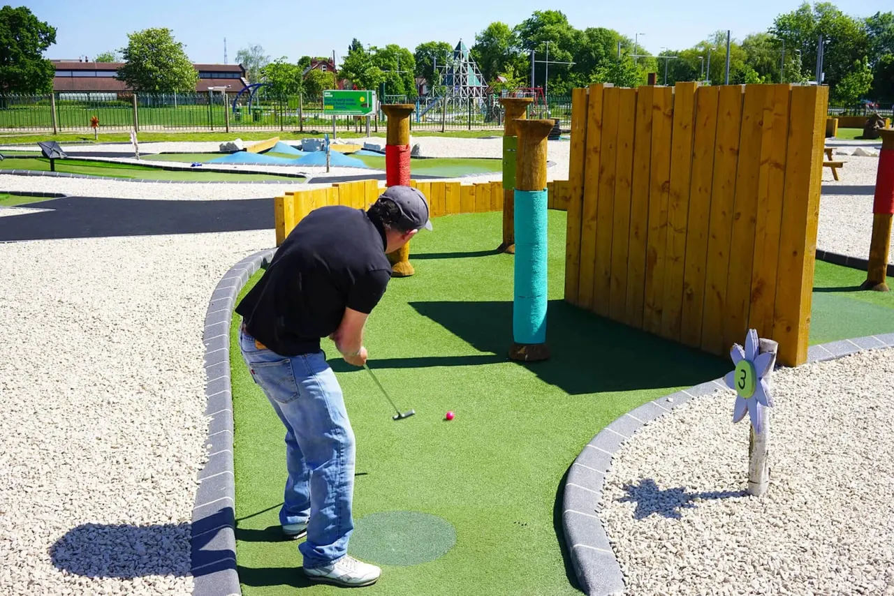 A person playing mini golf on a themed green course with wooden obstacles and coloured posts.