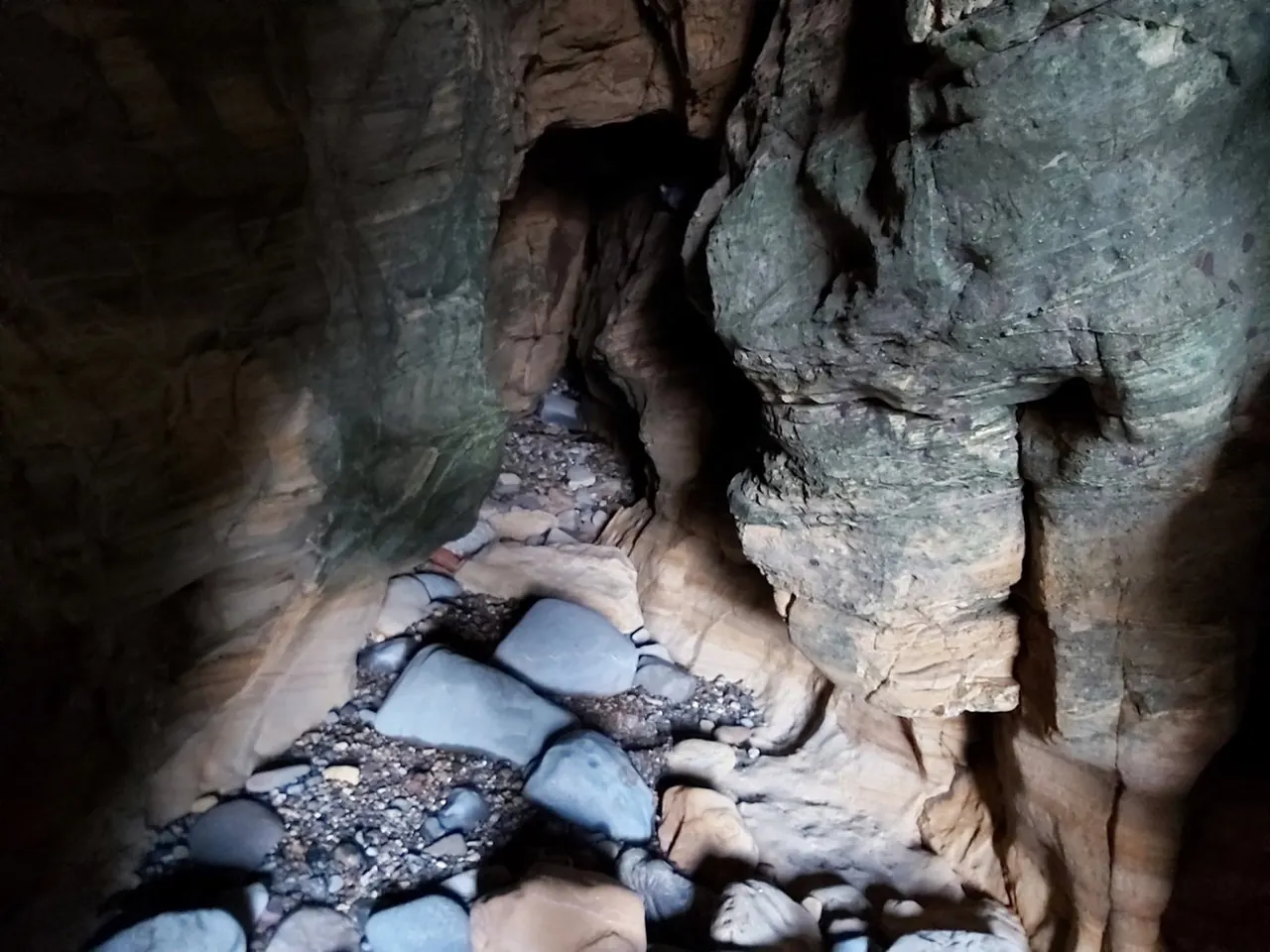 Interior of cave showing narrow rocky passageway with small stream and boulders on the floor.