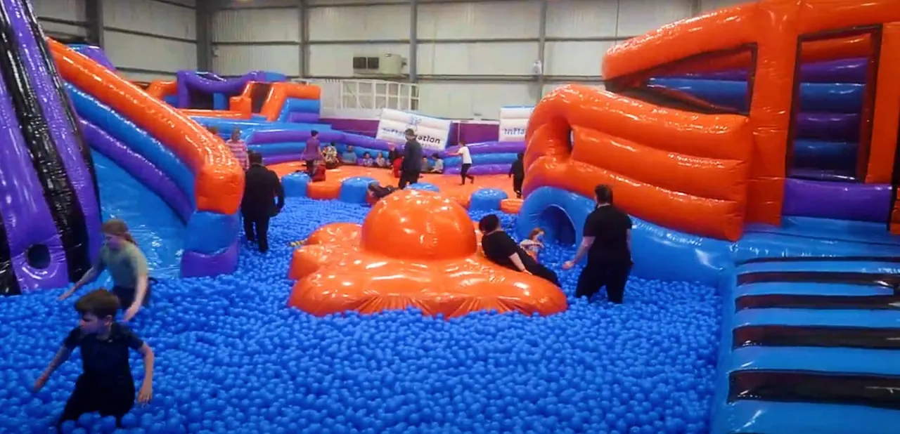 Children playing in an indoor soft play area with bright orange and blue inflatable structures and ball pit.