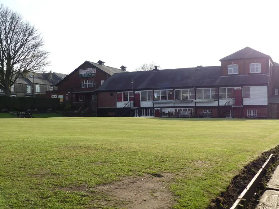 Large grass playing field in front of red-brick sports pavilion building with bare winter trees.