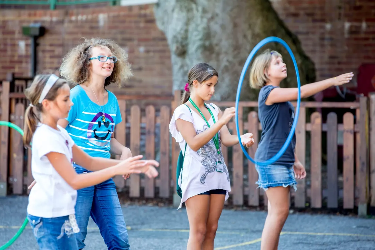 Four children playing with hula hoops in a brick-walled outdoor courtyard.