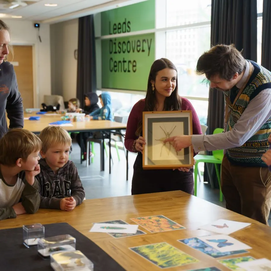 An educator shows young children a framed insect specimen during a hands-on discovery session at an indoor learning centre.