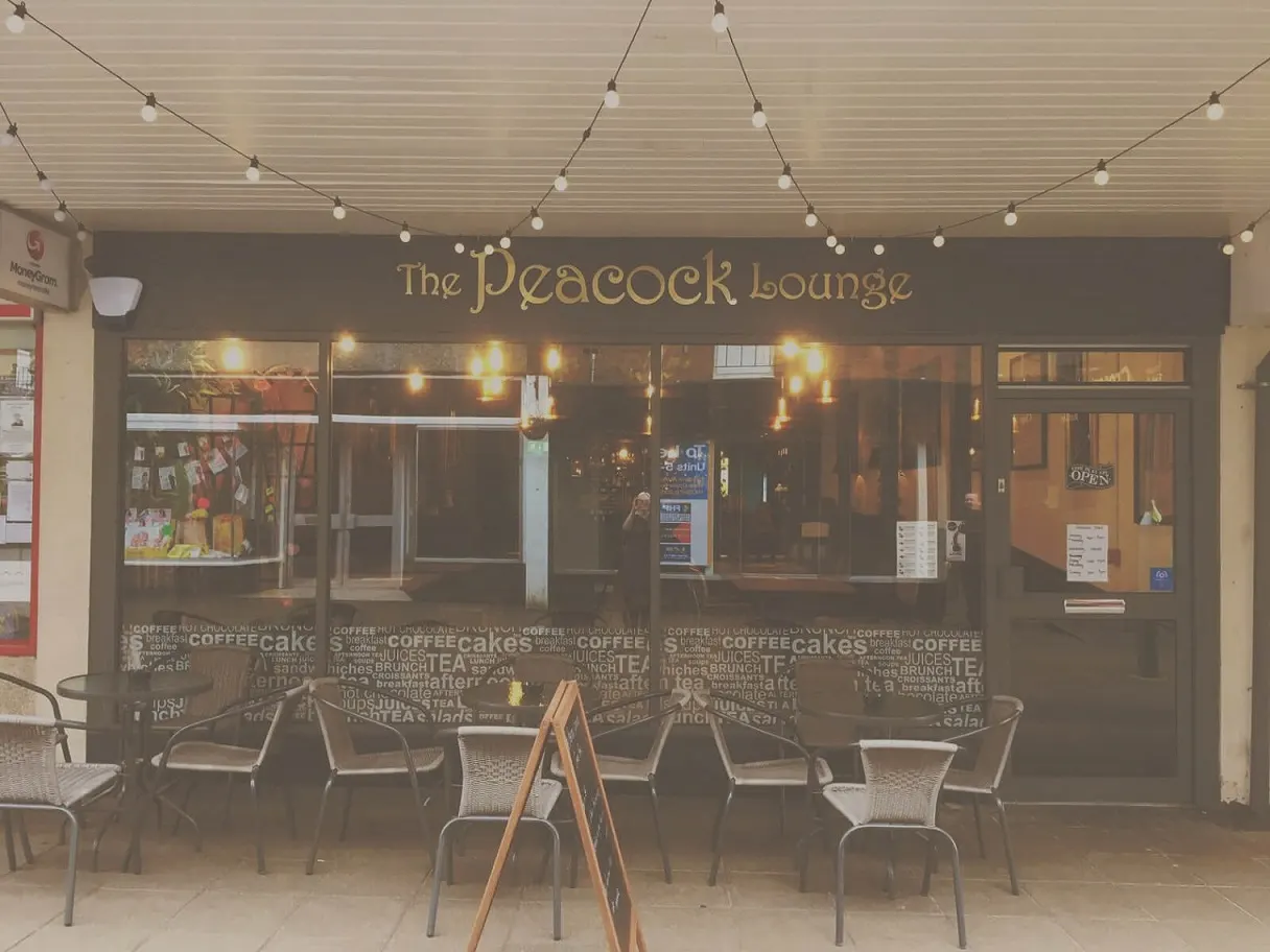 The Peacock Lounge café frontage at dusk with outdoor seating and warm string lighting overhead.