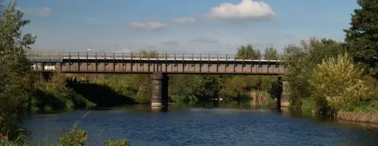 A footbridge and cycle path spanning a river lined with trees and vegetation.
