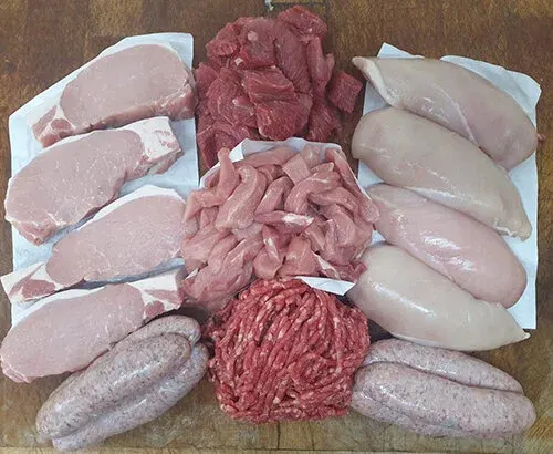Various raw meat cuts including pork chops, chicken breasts, beef and sausages arranged on white paper.