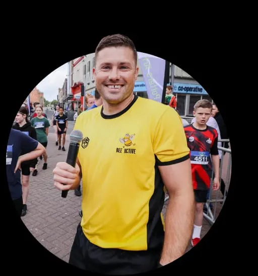 Man in yellow Bee Active t-shirt smiling at a community running event on a high street.