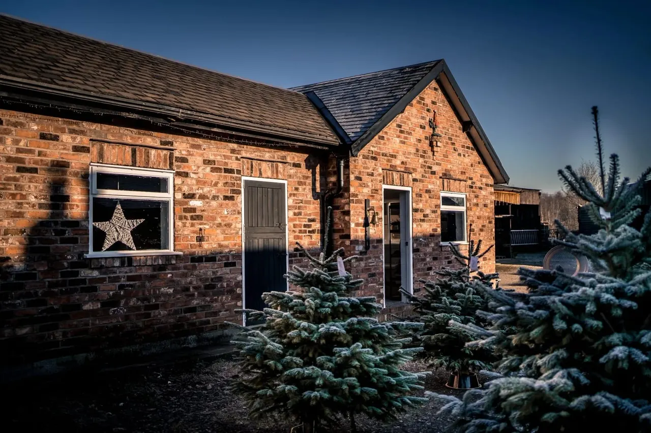 Red brick building with black doors and windows, decorated with a large star, surrounded by evergreen shrubs on a clear day.