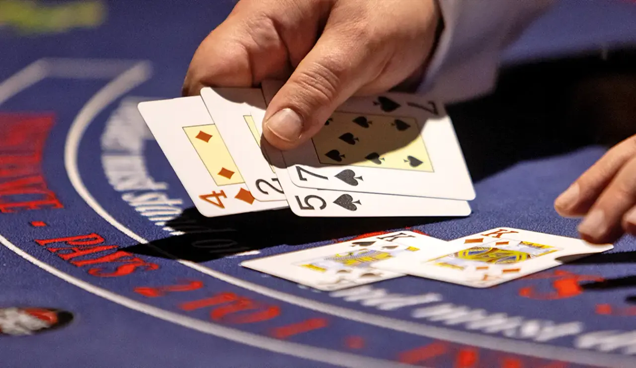 Dealer's hands revealing playing cards during a game of poker on a blue casino table.