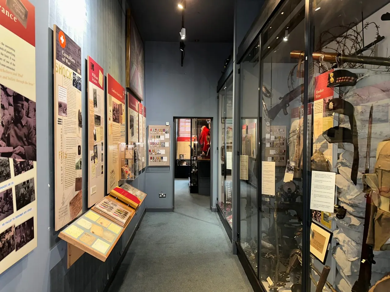 Museum corridor displaying military history exhibits with informational panels on walls and uniforms and weapons in glass cases.