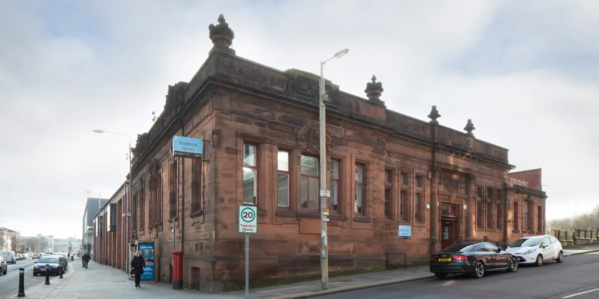 Victorian sandstone library building with ornamental roof turrets on a street corner with parked cars.